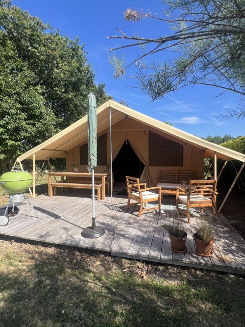 Tente de glamping en toile avec terrasse en bois, espace patio meublé et parasol vert aux Gîtes De L'odet