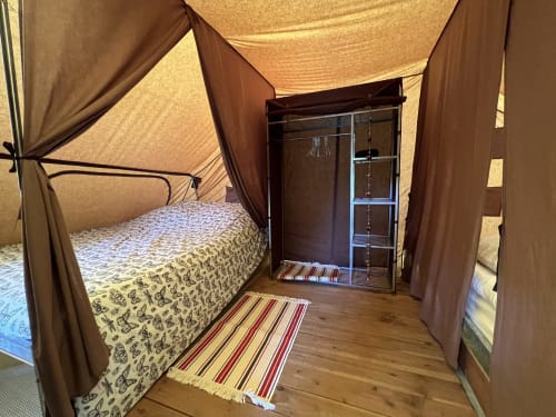 Chambre cosy des Gîtes De L'odet avec lit à baldaquin, armoire en bois et tapis rayé à Clohars-Fouesnant