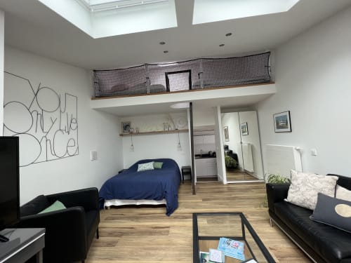 Studio moderne aux Gîtes De L'odet : lit bleu, assises noires, kitchenette et mezzanine