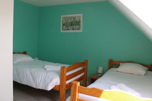 Twin beds with wooden frames and white linens in bright turquoise bedroom at Domaine des Piéris, Grandcamp-Maisy
