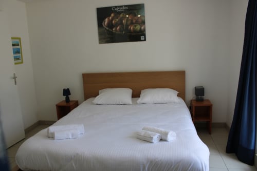 Spacious bedroom at Domaine des Piéris cottage with queen bed, white linens, wooden headboard, and garden view in