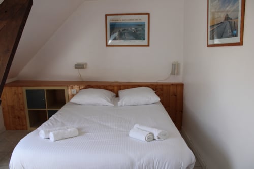 Comfortable double bed with white linens and rolled towels in a wood-paneled bedroom at Domaine des Piéris, Grandcamp-Maisy