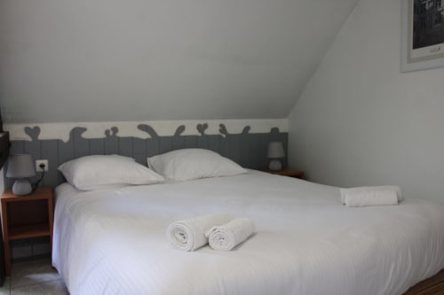 Cozy bedroom at Domaine des Piéris with white bedding, two pillows, rolled towels, wooden nightstand, and decorative