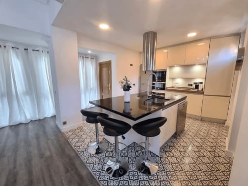Cocina y comedor modernos en CTH Granada con isla negra, gabinetes color crema y piso con patrón