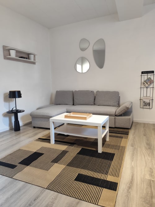 Salon contemporain de l'appartement Accolade à Châteaudun avec canapé gris, table blanche et tapis géométrique