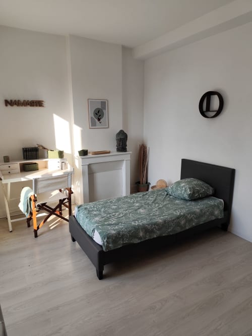 Chambre moderne à l'appartement Accolade à Châteaudun avec lit noir, parure verte motifs, bureau blanc et décoration épurée