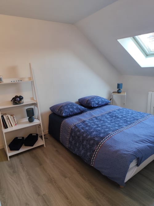 Chambre mansardée moderne à Accolade Châteaudun avec literie bleue, étagères blanches, lucarne et parquet