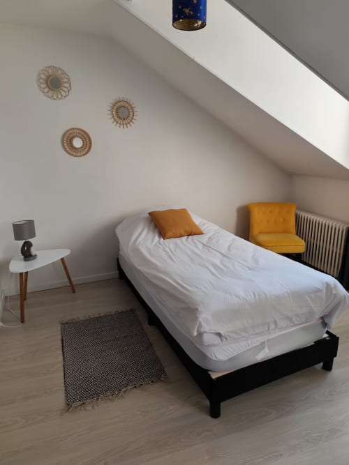 Chambre lumineuse sous les combles aux appartements Accolade à Châteaudun avec lit simple, fauteuil moutarde et décoration murale
