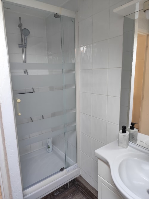 Salle de bains moderne de l'appartement Accolade à Châteaudun avec douche vitrée et carrelage blanc