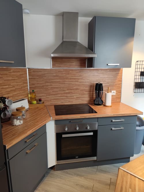 Cuisine moderne de l'appartement Accolade à Châteaudun avec plans de travail en bois, meubles gris et appareils électroménagers en inox