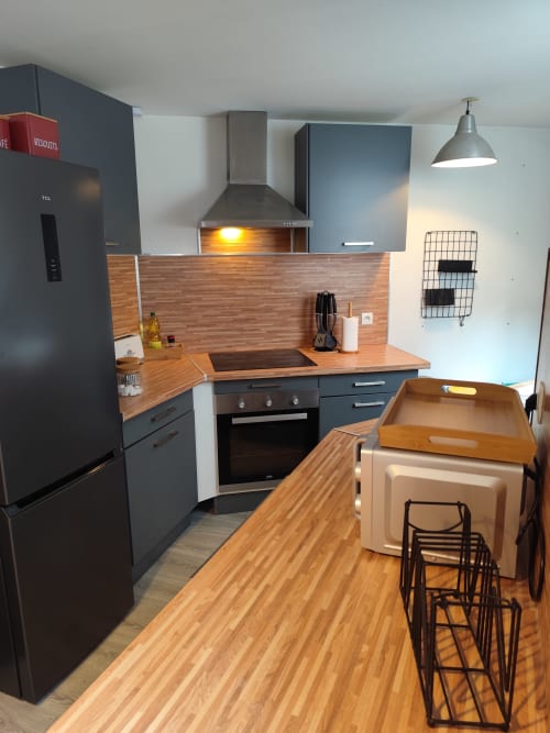 Cuisine moderne de l'appartement Accolade Châteaudun avec armoires sombres, comptoirs en bois et électroménagers en acier inoxydable