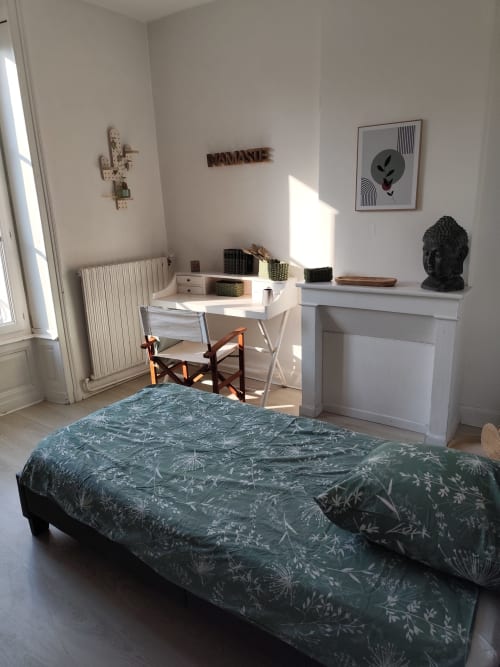 Chambre lumineuse de l'appartement Accolade à Châteaudun avec literie botanique verte, bureau de travail, cheminée et décoration minimaliste
