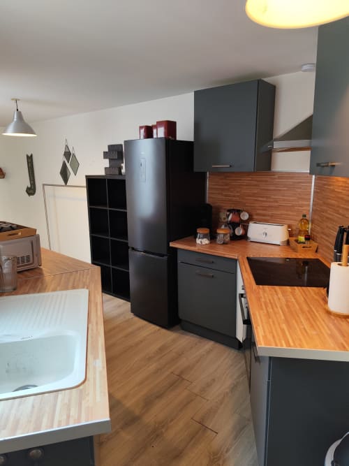 Cuisine moderne de l'appartement Accolade avec armoires noires, plan de travail en bois, réfrigérateur inox et sol en bois