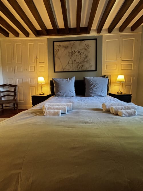 Chambre luxueuse au Le Prieuré Du Preux avec oreillers bleus, serviettes roulées, poutres apparentes et vue sur le jardin