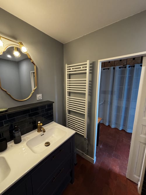 Salle de bains moderne avec porte-serviettes blanc, carrelage noir, accessoires dorés et miroir au Prieuré Du Preux