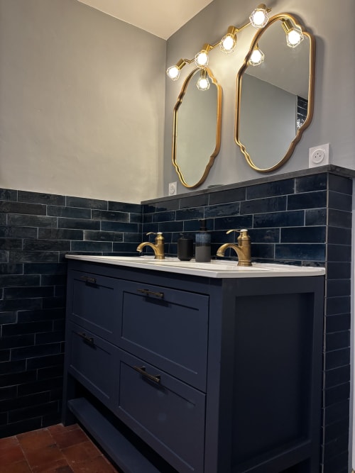 Vanité de salle de bain moderne avec robinetterie dorée double, dosseret en carrelage noir et miroirs rétroéclairés au Prieuré Du Preux