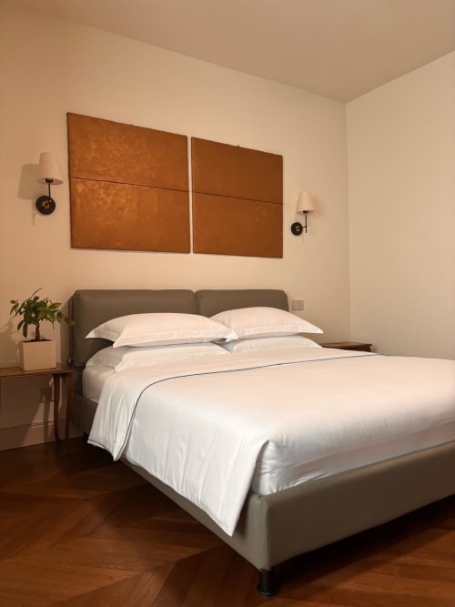 Camera moderna del B&B Delta Majestic a Pordenone con letto imbottito grigio, biancheria bianca, arte murale in rame e pavimenti in legno
