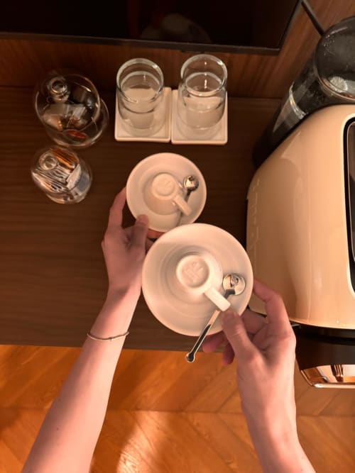 Ospite con tazza di tè bianca e piattino al B&B Delta Majestic di Pordenone, con bicchieri d'acqua e amenità dell'hotel su tavolo in legno