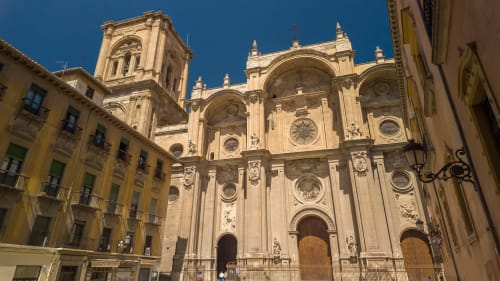Granada Cathedral's ornate baroque facade with golden stone, historic buildings, and clear blue sky in Granada, Spain