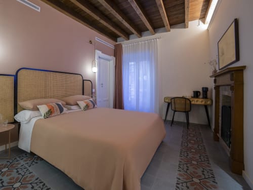 Retro bedroom at YOUnique Boutique Rooms Milano with rattan headboard bed, exposed wooden beams, desk, and city view curtains