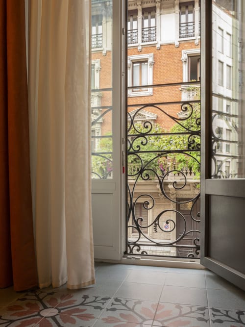 Modern bedroom with French doors opening to Parisian-style balcony overlooking Milan's brick architecture, YOUnique Boutique