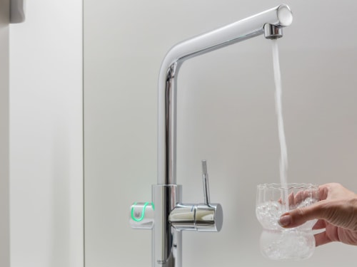 Moderno rubinetto cromato con acqua che scorre in un bicchiere presso YOUnique Boutique Rooms Milano
