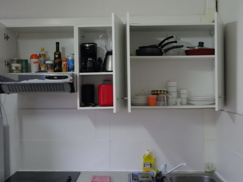 Open kitchen cabinets with cookware, dishes, and pantry items in Studio Face Marina apartment, Saint-François