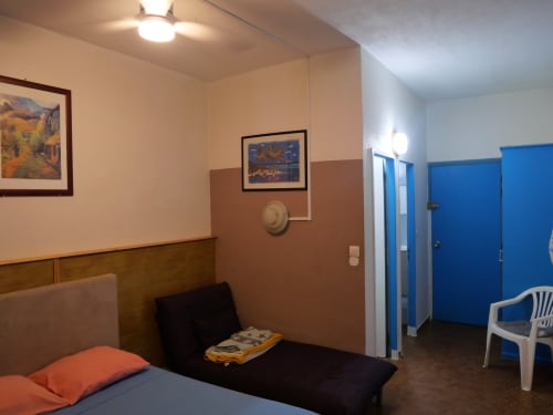 Studio apartment bedroom with bed, fan, artwork, and blue bathroom doors at Studio Face Marina, Saint-François