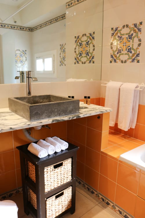 Salle de bains luxueuse de l'Hôtel Villa Roseraie avec lavabo en pierre, carrelage orange, assiettes décoratives et serviettes pliées