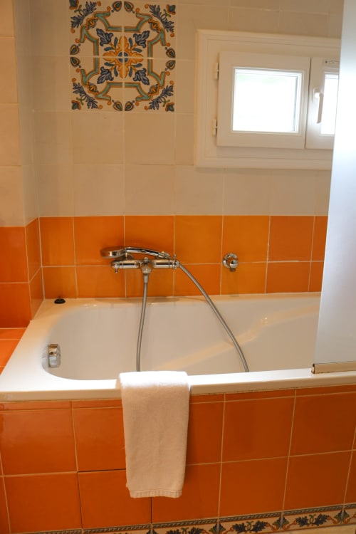 Salle de bains moderne à l'Hôtel Villa Roseraie à Vence avec baignoire blanche, robinetterie chromée, carrelage orange vibrant et éléments décoratifs