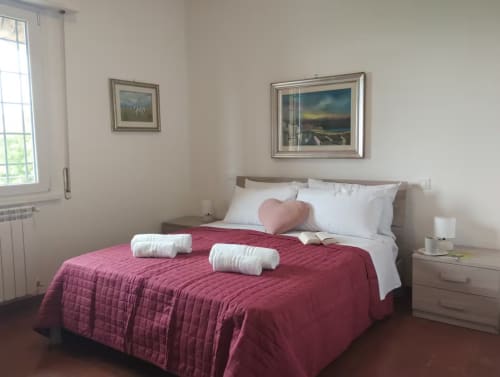 Camera moderna con trapunta trapuntata bordeaux, cuscini bianchi e cuscino a cuore a Casa gli Archi sul Borgo di Campagnano di
