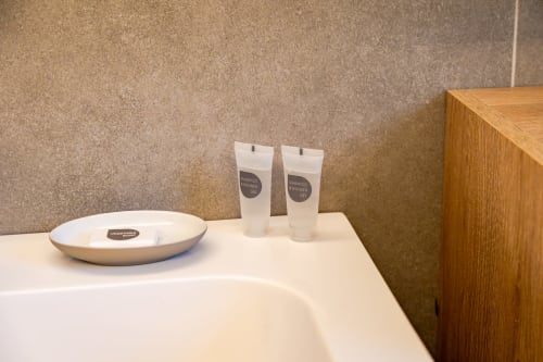 Servizi da bagno presso Treviso Stays: ciotola in ceramica bianca, due bottiglie di shampoo sul bancone del lavabo con parete piastrellata beige