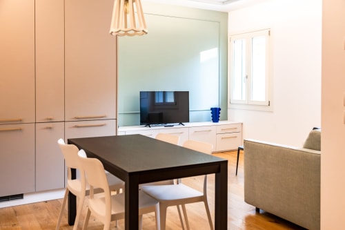 Zona pranzo suite moderna presso Treviso Stays con tavolo nero, sedie bianche, mobili in legno chiaro e vista sulla città