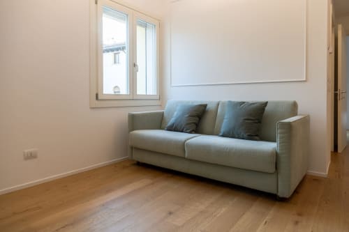 Elegante divano beige con cuscini blu in luminoso soggiorno di Treviso Stays, con pavimenti in legno e vista sulla città