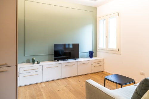 Soggiorno moderno della suite Ca' Borsa IV a Treviso Stays con mobili bianchi, TV, pavimenti in legno e specchio con vista sulla città