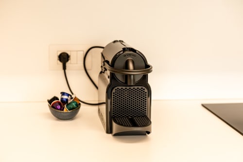 Macchina da caffè Nespresso nera su scrivania bianca nell'appartamento Treviso Stays, con portacapsule e presa a muro visibili
