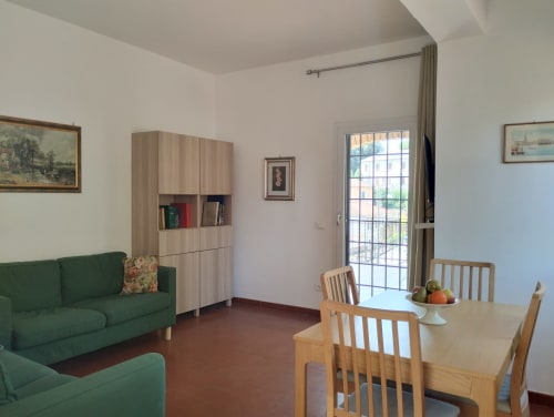 Luminoso soggiorno a Campagnano di Roma con divani verdi, tavolo da pranzo in legno, credenza e accesso alla terrazza