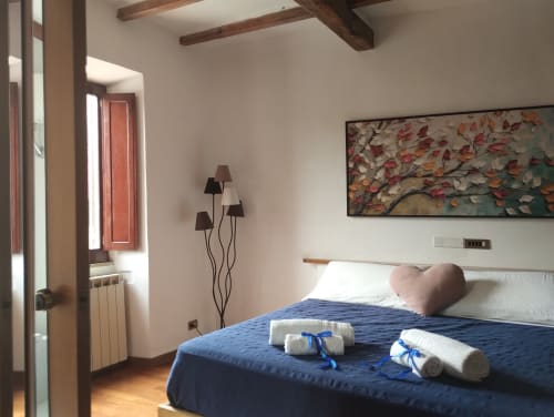 Camera luminosa presso Casina Bella Vista a Campagnano di Roma con biancheria blu, cuscini bianchi, travi in legno e quadri