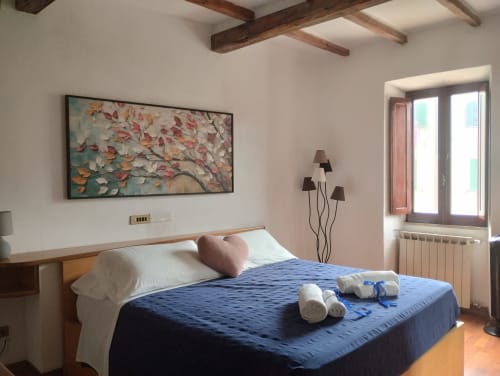 Camera moderna a Casina Bella Vista con letto blu, travi in legno, quadri con foglie autunnali e accesso al balcone a Campagnano di