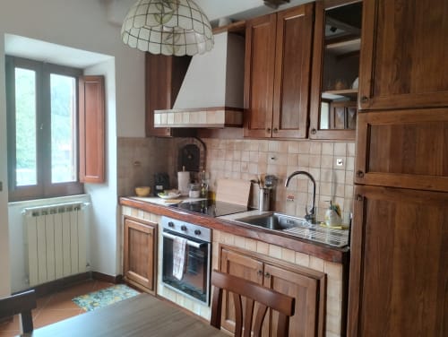 Cucina in legno con rivestimento in piastrelle color crema, lavello in acciaio inox, forno a gas e lampada a sospensione color crema nella Casina Bella Vista