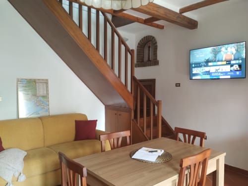 Ampio soggiorno nell'appartamento Casina Bella Vista con divano giallo, scala in legno, tavolo da pranzo, TV a schermo piatto e