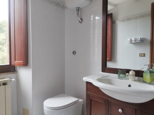 Moderno bagno di Casina Bella Vista a Campagnano di Roma con piastrelle bianche, mobile in legno, lavabo curvo e vetro