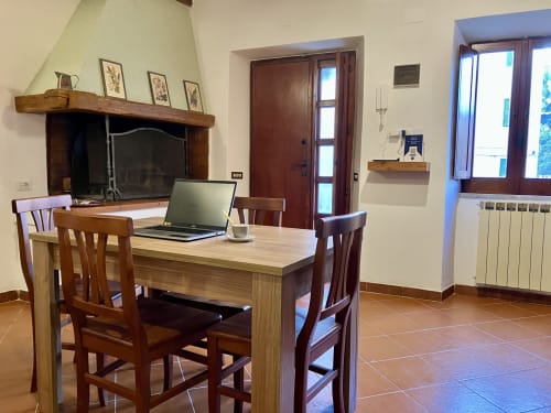 Ampia zona pranzo con tavolo e sedie in legno, laptop, camino e porte che si aprono sul balcone di Casina Bella Vista