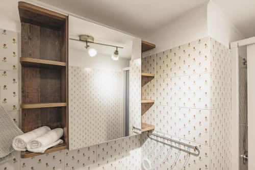 Bagno moderno con carta da parati floreale, scaffali in legno, specchio e asciugamani bianchi arrotolati a Casa Pettinari, Roma