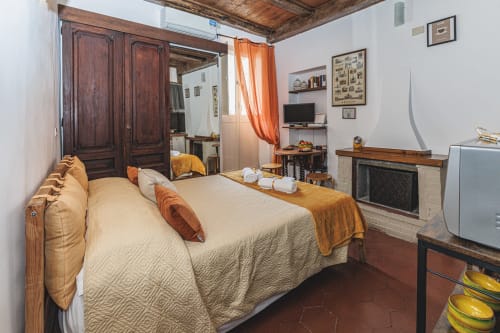 Camera rustica a Casa Pettinari 78 a Campagnano di Roma con soffitto in travi di legno, letto matrimoniale, camino e vista sulla città.