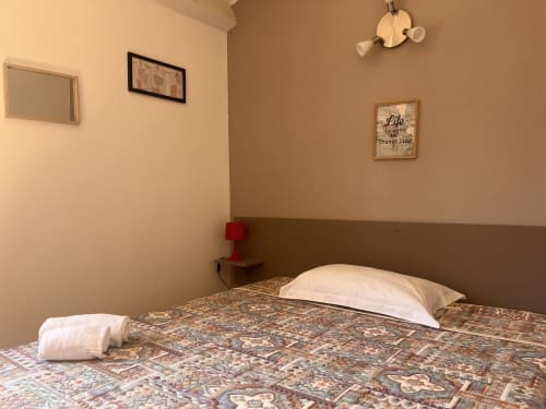 Camera d'hotel al Le Maquis Plage a Poggio-Mezzana con biancheria a fantasia, cuscino bianco, lampada rossa e decorazioni murali a tema marino