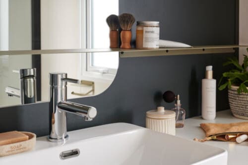 Lavabo de salle de bain moderne à l'hôtel Le Maquis Plage avec robinet chromé, mur sombre, miroir et produits de luxe