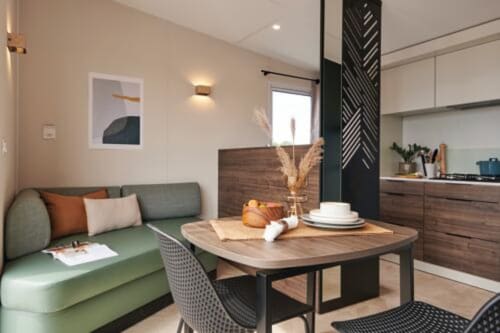 Studio moderne au Maquis Plage avec cuisine ouverte, coin repas, canapé vert et mobilier en bois à Poggio-Mezzana