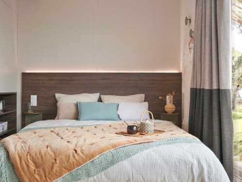 Chambre contemporaine de la villa Le Maquis Plage avec tête de lit en bois, touches bleues et vue sur le jardin