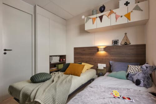 Chambre d'enfants moderne au Maquis Plage avec deux lits, tête de lit en bois, guirlandes colorées et rangements organisés